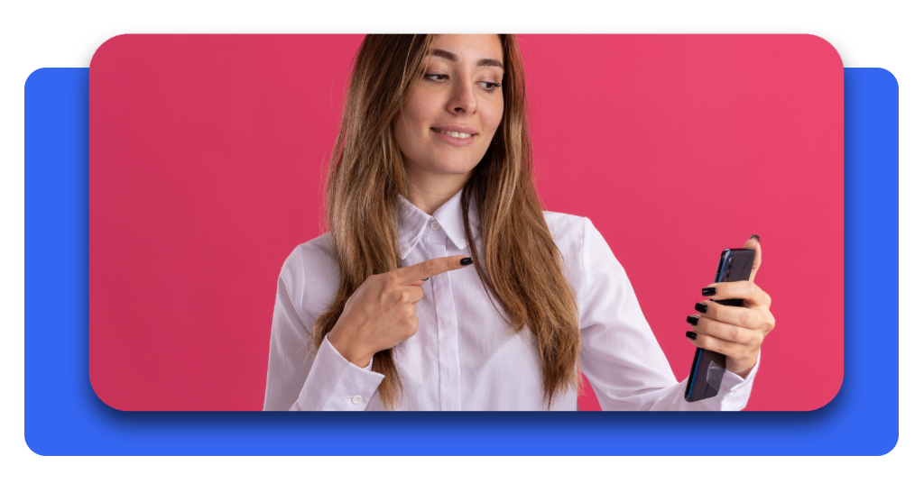 Joven mujer sonriente señalando la pantalla de su teléfono móvil para mostrar cómo bloquear llamadas molestas y proteger su privacidad de forma sencilla.